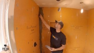 man spreading out mud in corner of incomplete walk-in shower