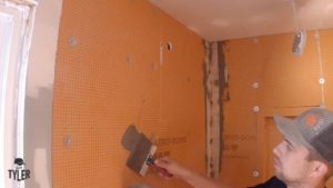 man applying mud to screw holes inside of incomplete walk-in shower